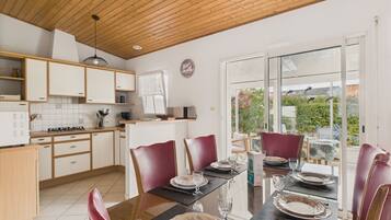 Une cuisine moderne avec des meubles en bois et un coin repas comprenant une table en verre et des chaises rouges.