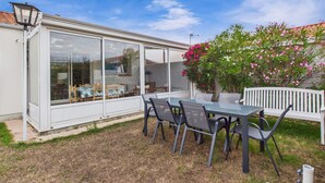 A covered patio with a table and chairs, a white bench, and a potted plant with pink flowers. - Garden and veranda - House 4 adults 2 children (Saint-Hilaire-de-Riez)