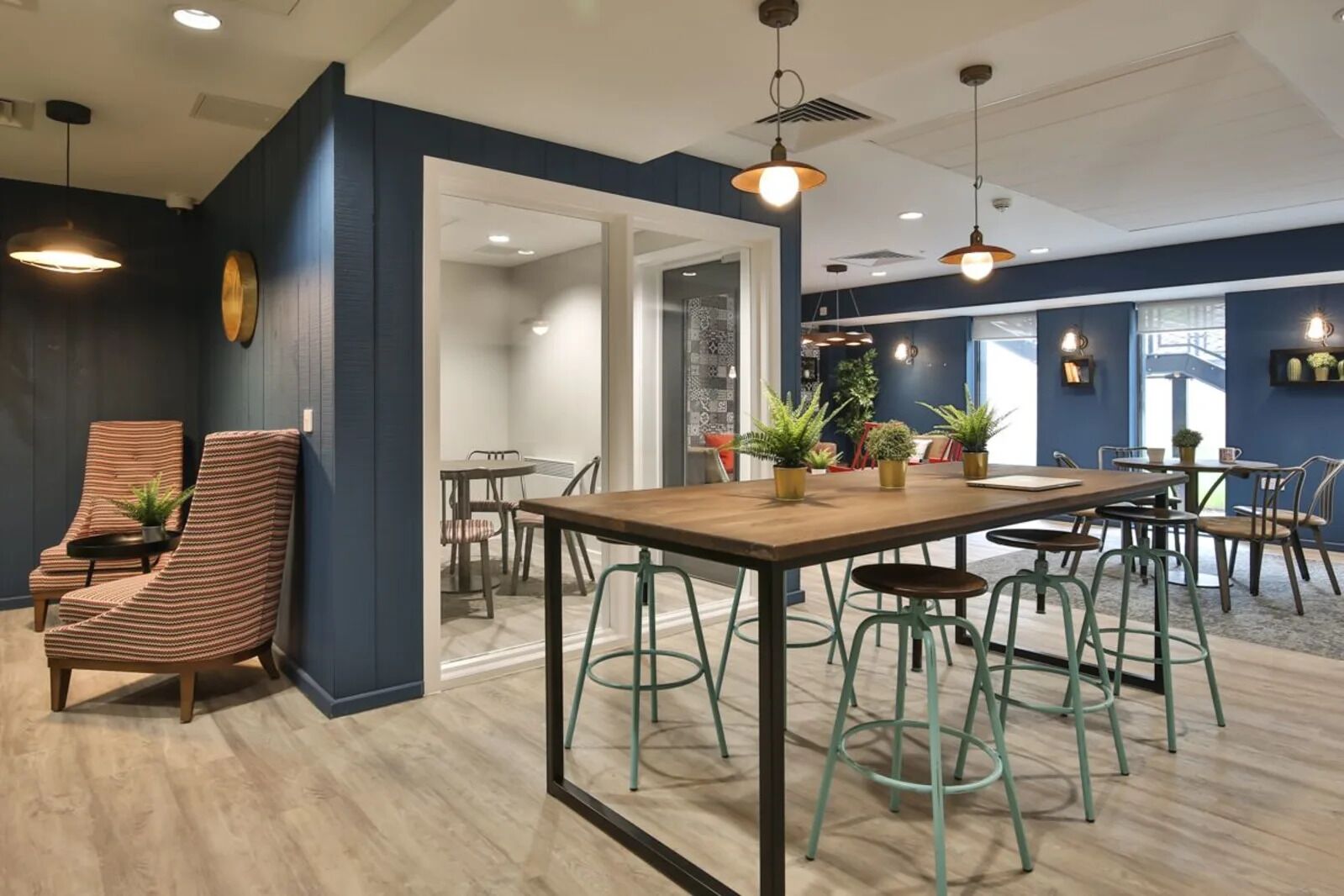 A modern interior with a wooden table and green stools, a striped chair, and potted plants.