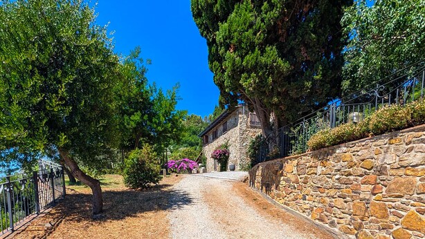 A stone building with a gravel path leading to it, surrounded by trees and a metal fence. - Villa Poggio al Coniglio at Suvereto with Pool (Suvereto)