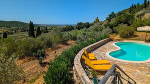 A pool with yellow lounge chairs and a stone deck, surrounded by greenery and hills. - Villa Poggio al Coniglio at Suvereto with Pool (Suvereto)