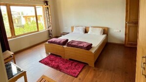 Une chambre avec un plafond en bois, un grand lit, un bureau en bois et une fenêtre donnant sur un paysage verdoyant.