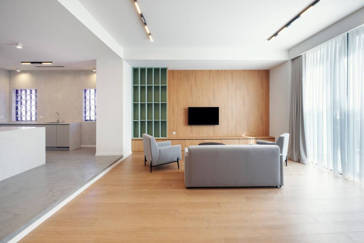 Een moderne woonkamer met een grijze bank, een houten accentmuur en een flatscreen televisie bevestigd boven een groen dressoir.