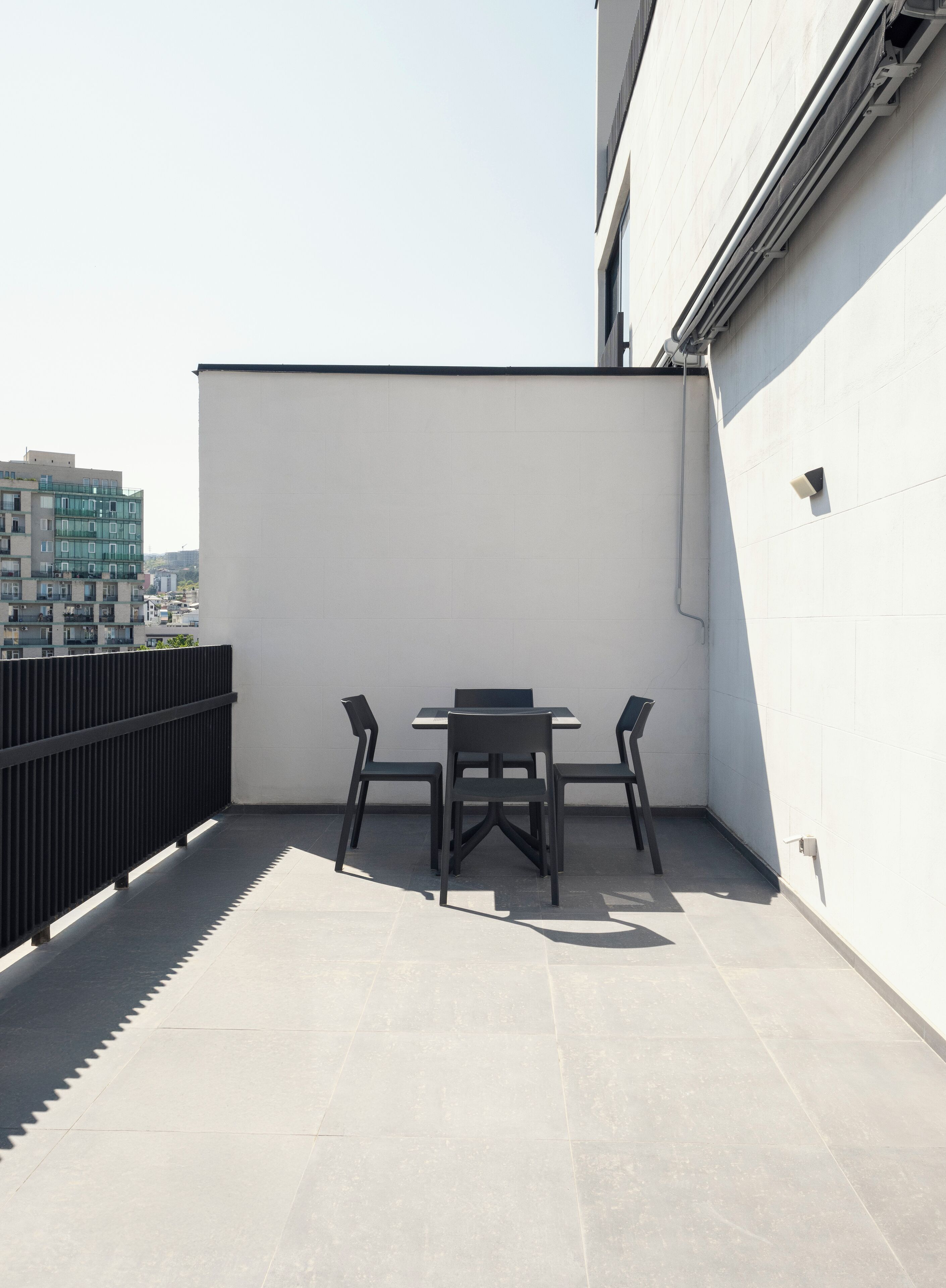 Una terraza en la azotea con una mesa, sillas, barandilla negra y pared blanca.