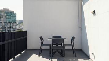 Una terraza en la azotea con una mesa, sillas, barandilla negra y pared blanca.