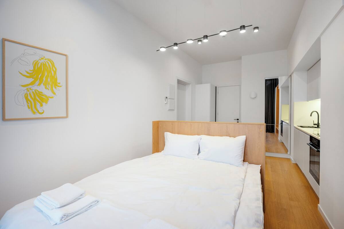 Een moderne hotelkamer met een groot bed, een houten hoofdbord en een keukenruimte zichtbaar door een open deur.