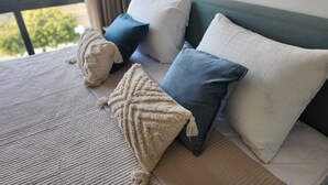 Una cama con un edredón color beige, dos almohadas y una almohada azul.