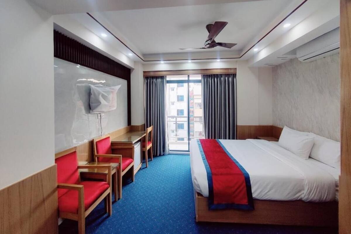 A hotel room with a bed, a desk, a chair, a ceiling fan, and a window with curtains.