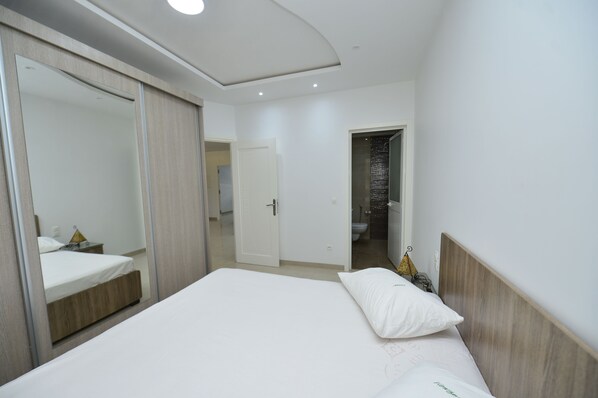 A modern hotel room with a large bed, a wardrobe, and a bathroom visible through an open door.