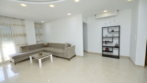 A modern living room with a beige sectional sofa, a white coffee table, and a black shelving unit with decorative items.