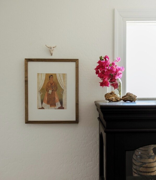 A framed picture on a wall, a vase with pink flowers, and a rustic object on a dark surface.