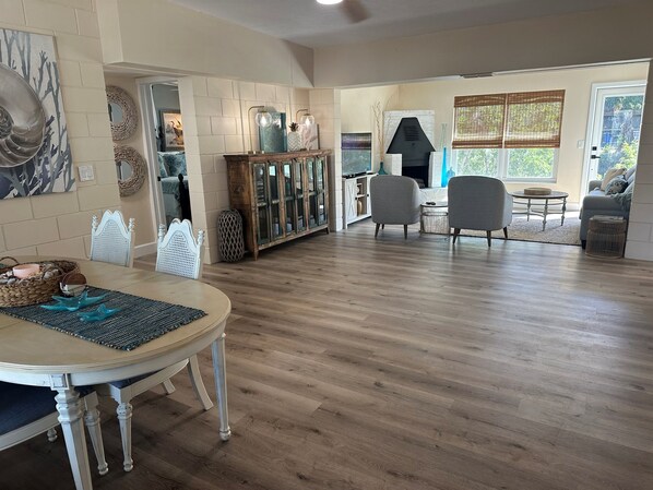 Un vaste espace de vie doté d’un plancher en bois, d’une table à manger avec des chaises, d’une cheminée et d’un coin salon comprenant un canapé et des fauteuils.