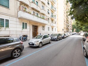Una calle bordeada de vehículos estacionados y un edificio con varios balcones.