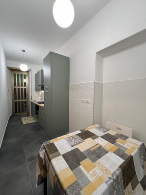 A compact hotel room with a bed, a small kitchenette, a bathroom, and a hallway leading to another room.