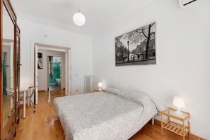 Une chambre à coucher comprenant un lit, une table de chevet avec une lampe, un tableau accroché au mur et une porte donnant sur une salle de bain.