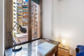 Une pièce avec un bureau, une lampe et une vue sur un immeuble à plusieurs étages doté de balcons.
