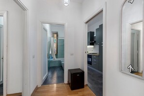 Een gang die leidt naar een badkamer met een douche en een klein zwart apparaat, mogelijk een verwarming, op de vloer.