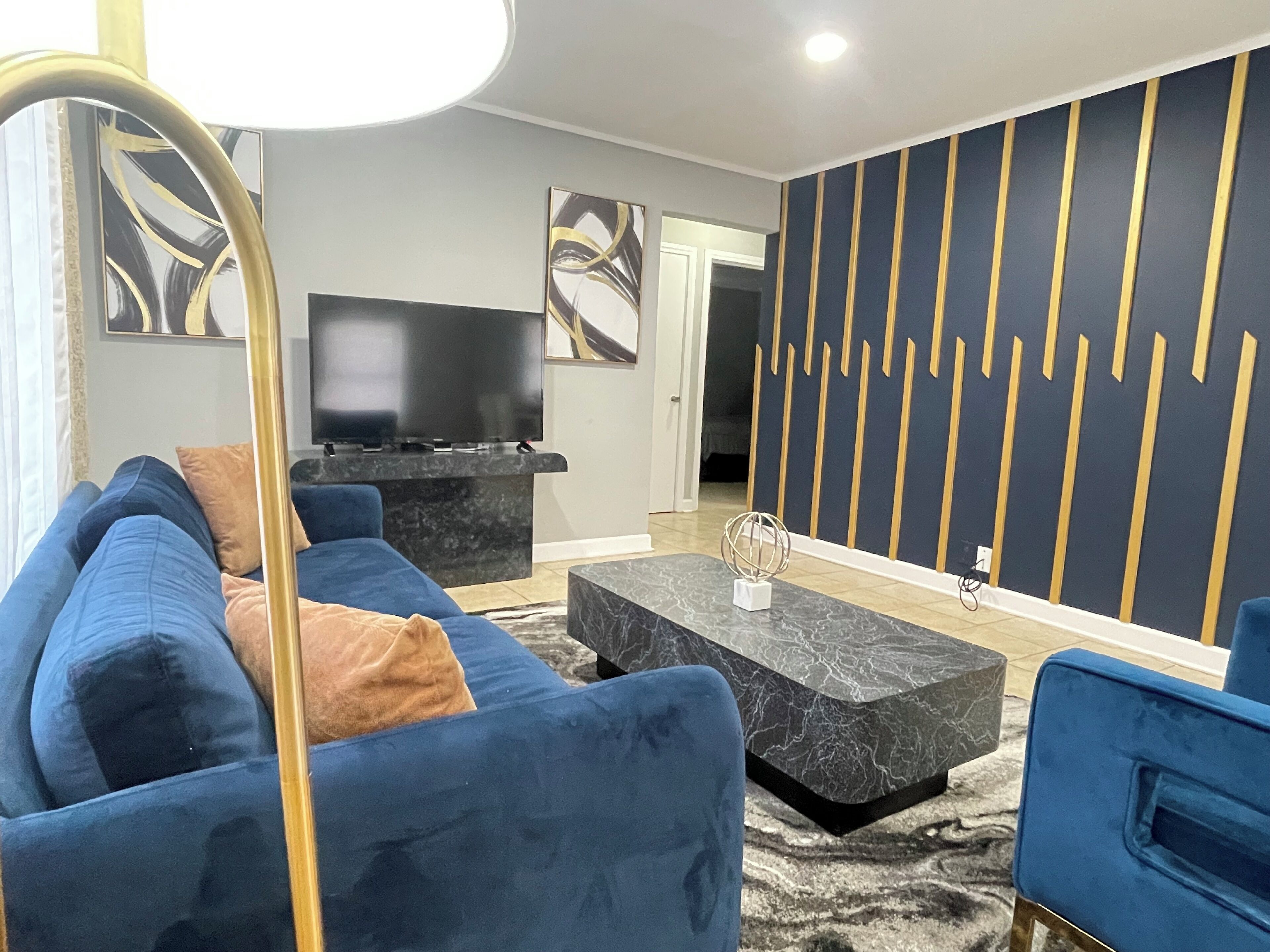 Un salon moderne avec un canapé bleu, un meuble de rangement noir pour appareils électroniques et une table basse en marbre.