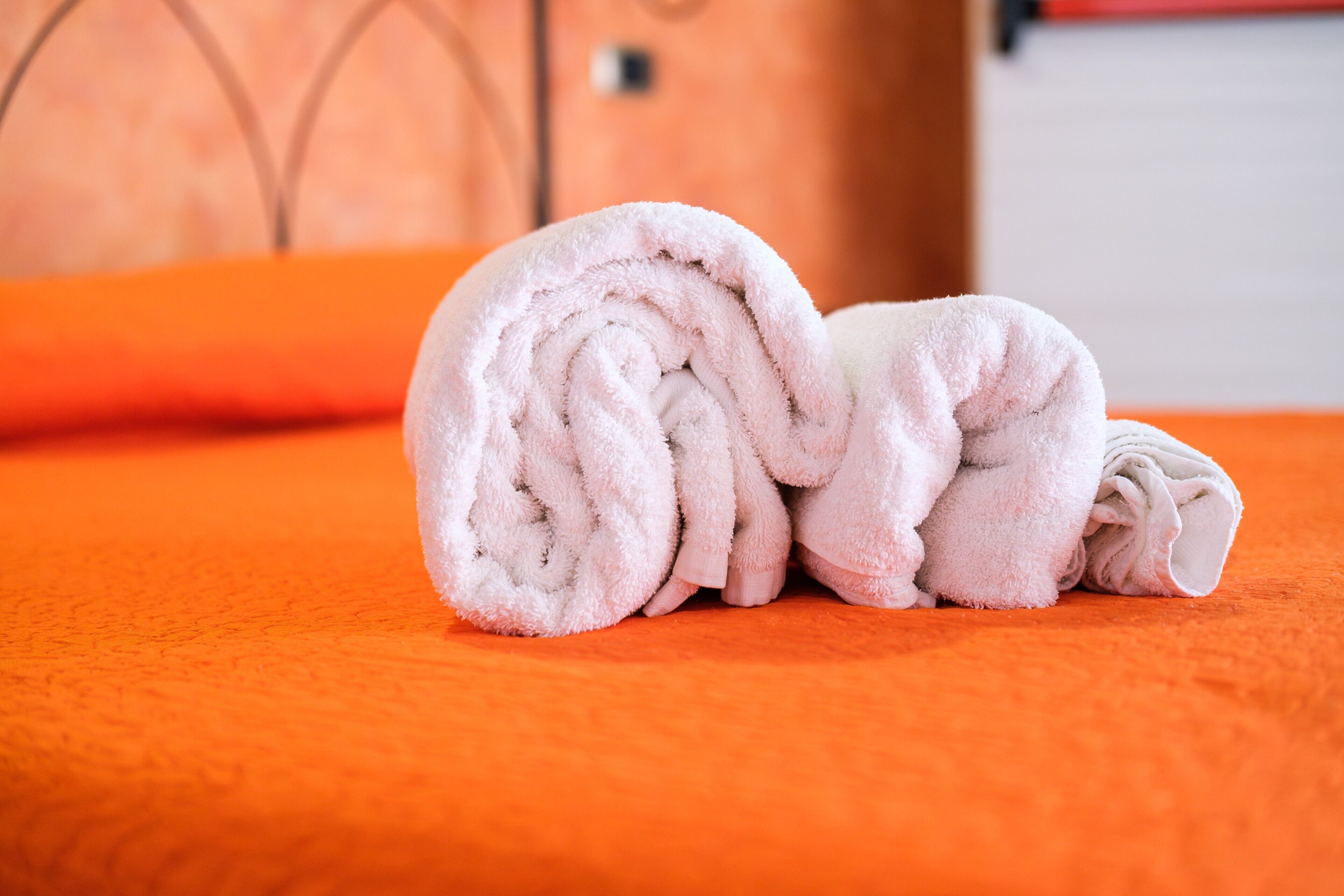 Una toalla enrollada sobre un edredón naranja en una habitación con cabecera de madera.