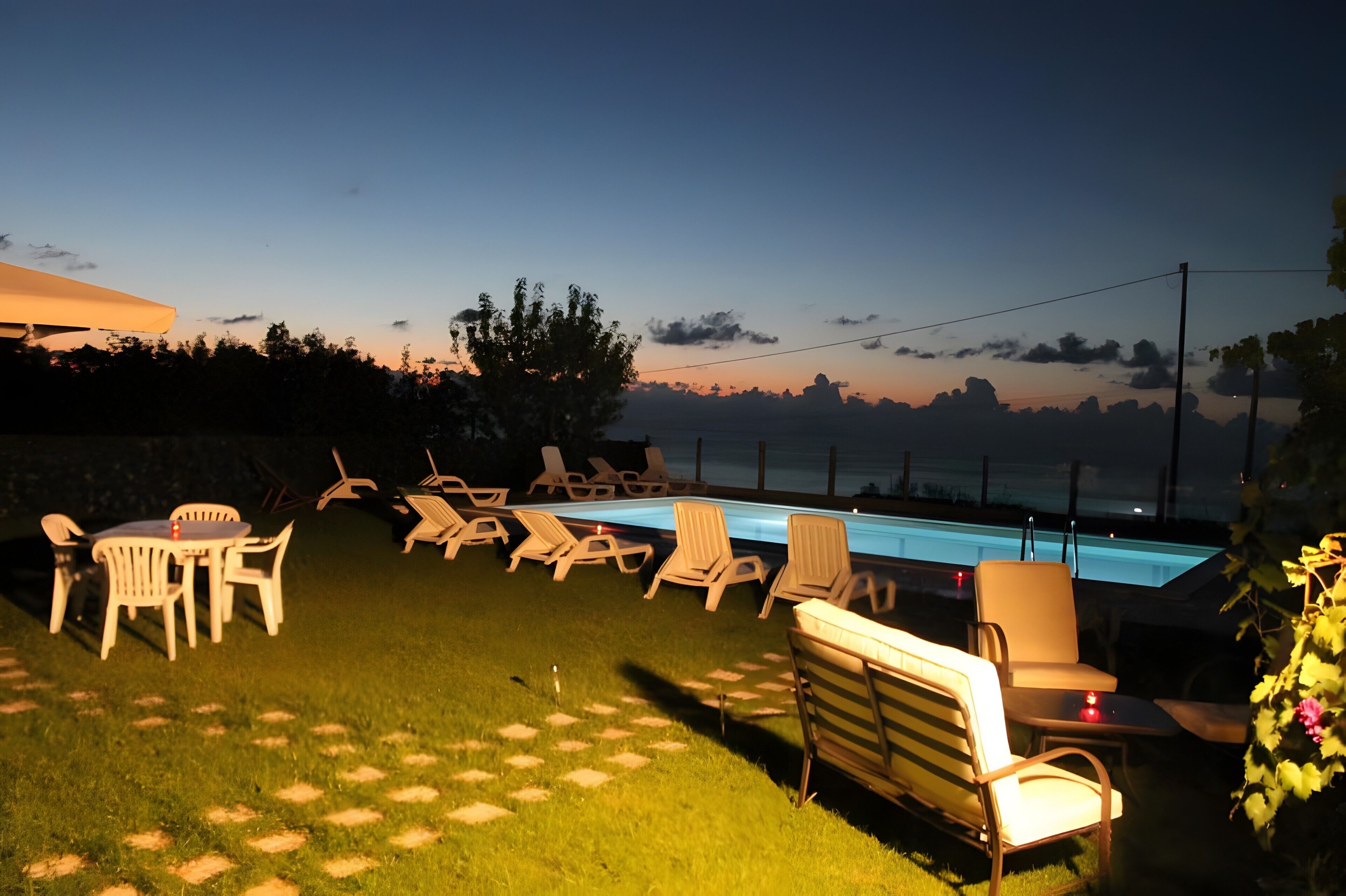 Un área junto a la piscina con sillones de descanso, una mesa y un césped.