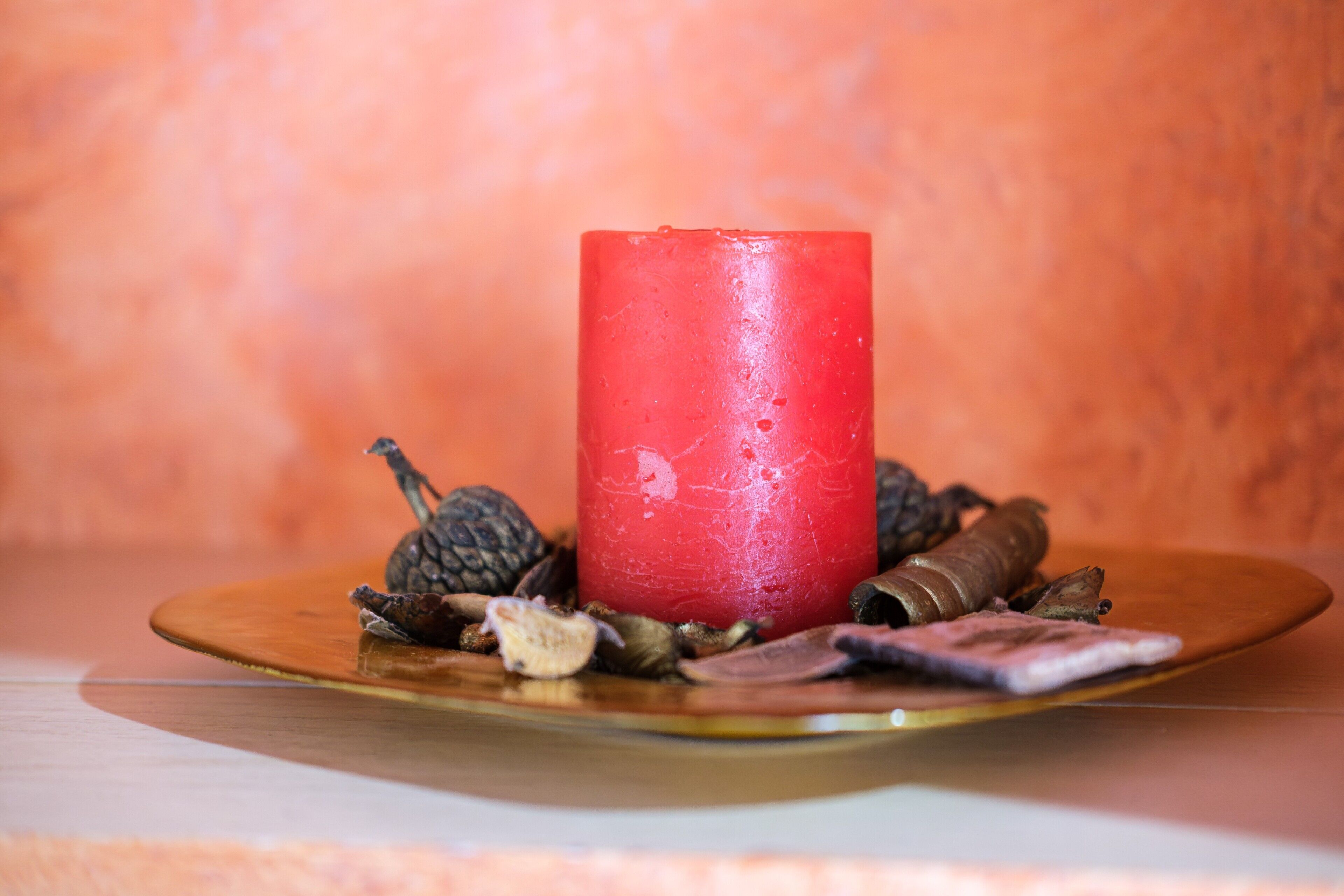 Une bougie rouge posée sur une assiette en bois, entourée de fleurs et d’herbes séchées.