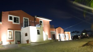 A multi-story residential building with a balcony, a well-lit entrance, and a driveway.