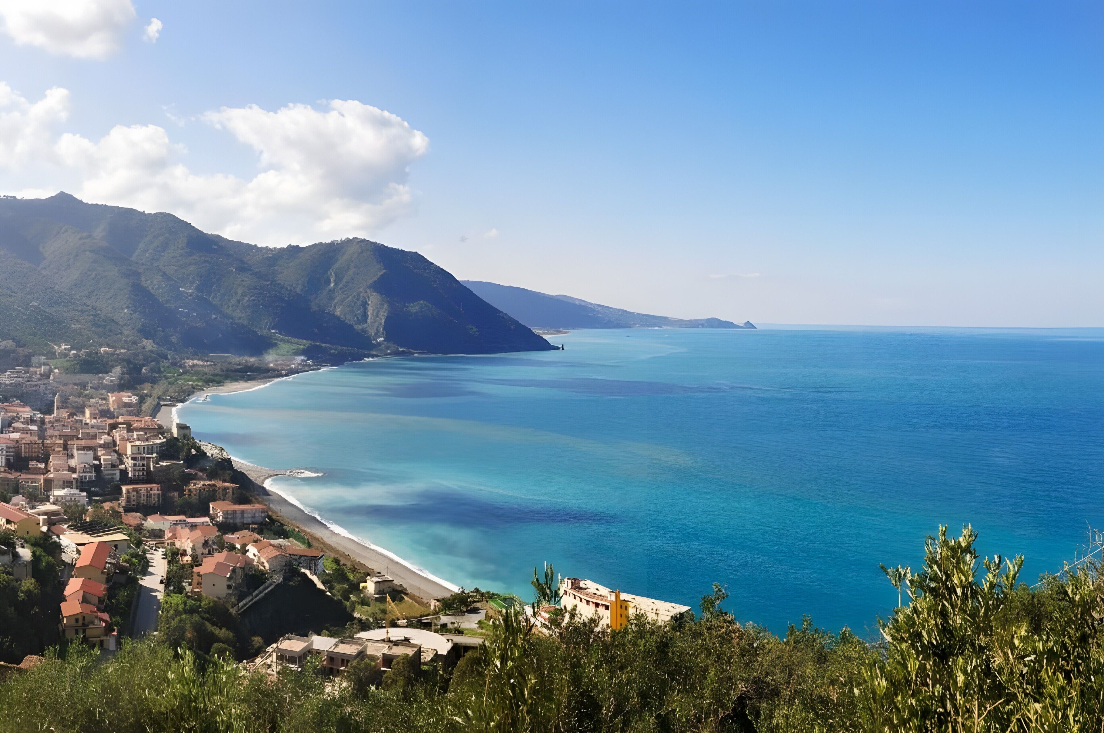 Una località costiera con spiaggia, edifici e montagne.