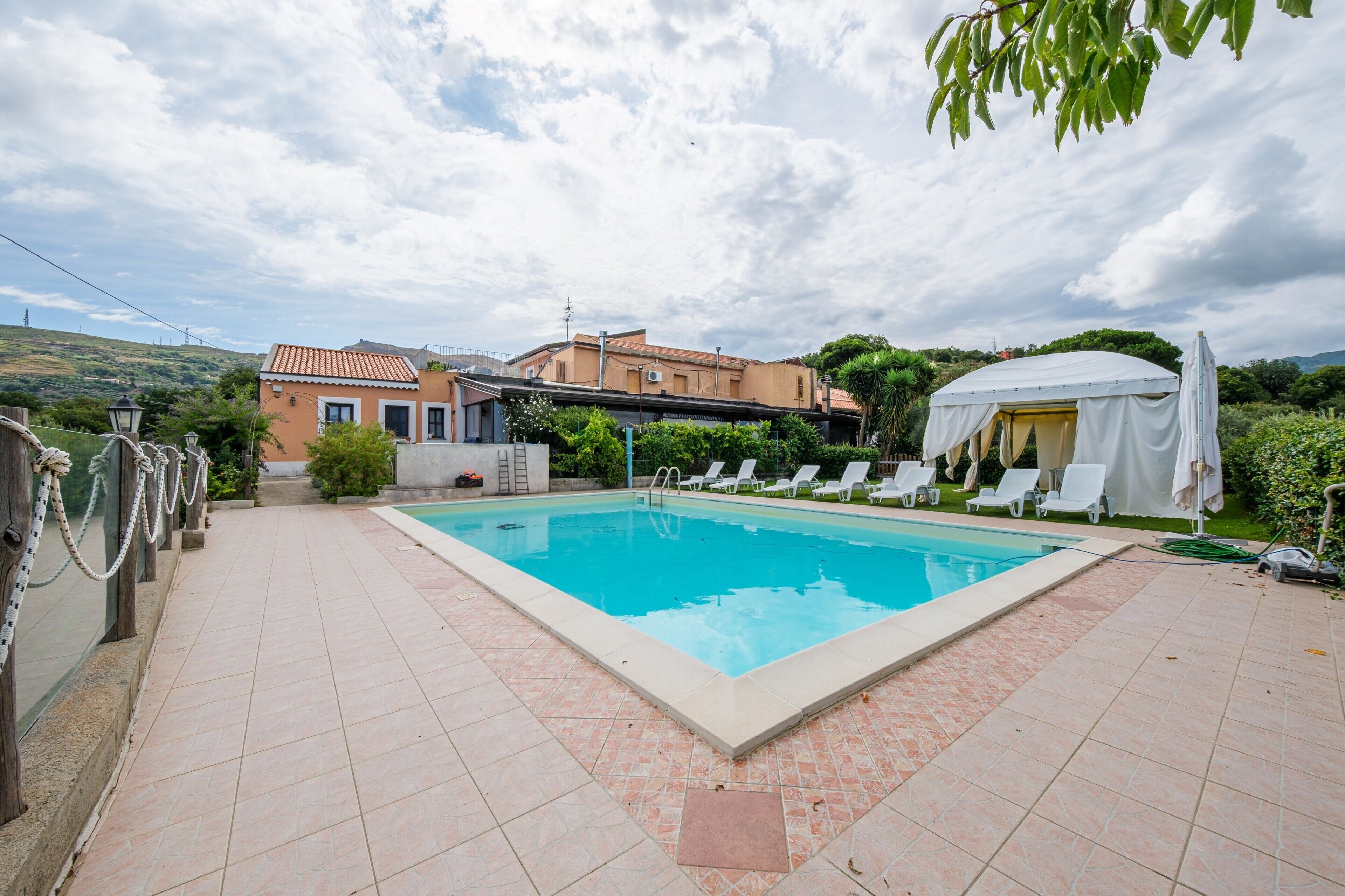 A swimming pool with lounge chairs, a tent, and a building in the background.