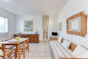 A room with a dining table, chairs, a sofa, a TV, a painting, and a mirror. - Apartment 'Trande' with Balcony, Wi-Fi and Air Conditioning (Santa Maria di Leuca)