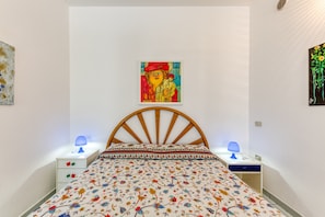 Een slaapkamer met een houten hoofdbord, een bloemenbedekking, twee nachtkastjes met lampen en een schilderij aan de muur.
