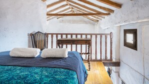 A bedroom with a wooden ceiling, a bed with a blue bedspread, two white towels, a wooden nightstand, and a window. - La Prensa Attic (Sorvilán)