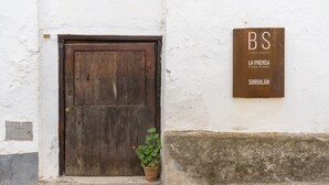 A rustic wooden door, a potted plant, and a sign with 'BS' and 'SORVILÁN' on a white wall. - La Prensa Attic (Sorvilán)
