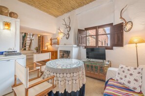 A cozy living room with a fireplace, a round table with a lace tablecloth, a sofa with a striped blanket, and a wall-mounted deer head decoration. - La Prensa Attic (Sorvilán)