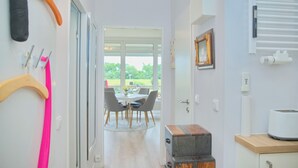 A hallway leading to a dining area with a view of the outdoors. There are clothes hanging on a rack, a framed picture on the wall, and a toaster on a counter. - House Baltic App. 97 incl. WLAN (Grömitz)