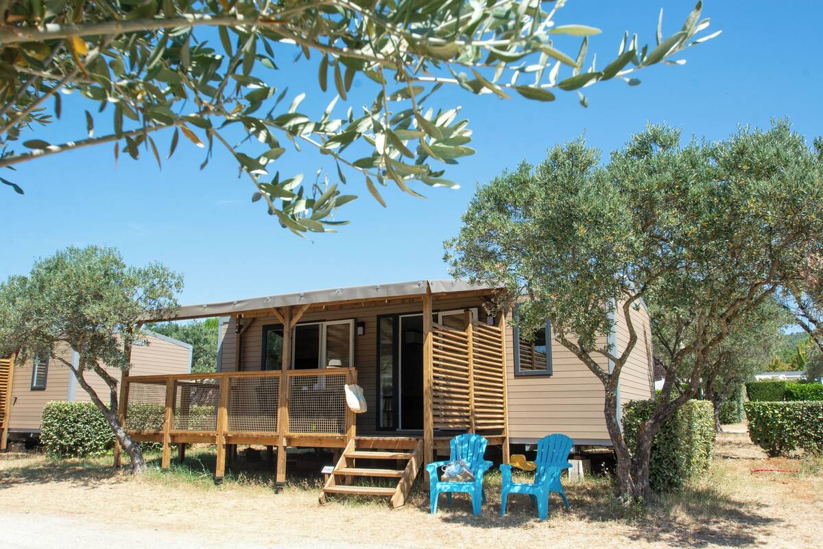 A wooden cabin with a porch, two blue chairs, and a small table.