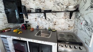 Une cuisine équipée d’une cuisinière, d’un évier et de meubles de rangement noirs. On y trouve des fruits et des légumes sur le plan de travail, et un four à micro-ondes au-dessus des meubles.