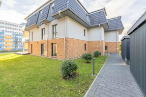 Een modern woongebouw met twee verdiepingen, een bakstenen gevel, een plat dak en een kleine voortuin met een pad en twee heggen.