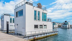 A modern waterfront building with large windows, a flat roof, and a dock extending into the water.