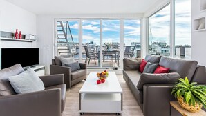 A modern living room with a white coffee table, grey sofas, and a large window offering a city view.