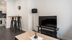 A modern living room with a TV, a coffee table, and a dining area with chairs.