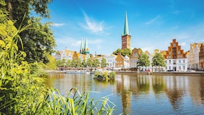 A riverside view of historic buildings with a prominent tower and spires, surrounded by lush greenery. - Modern apartment with exceptional sea view and balcony in Travemünde (Lübeck)