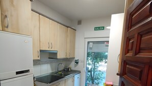 Una cocina con armarios de madera, un refrigerador blanco, un fregadero y una puerta con la etiqueta 'SALIDA'.