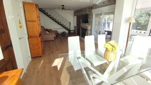 Una sala de estar moderna con una mesa de comedor de vidrio, un sofá, una chimenea y una escalera.
