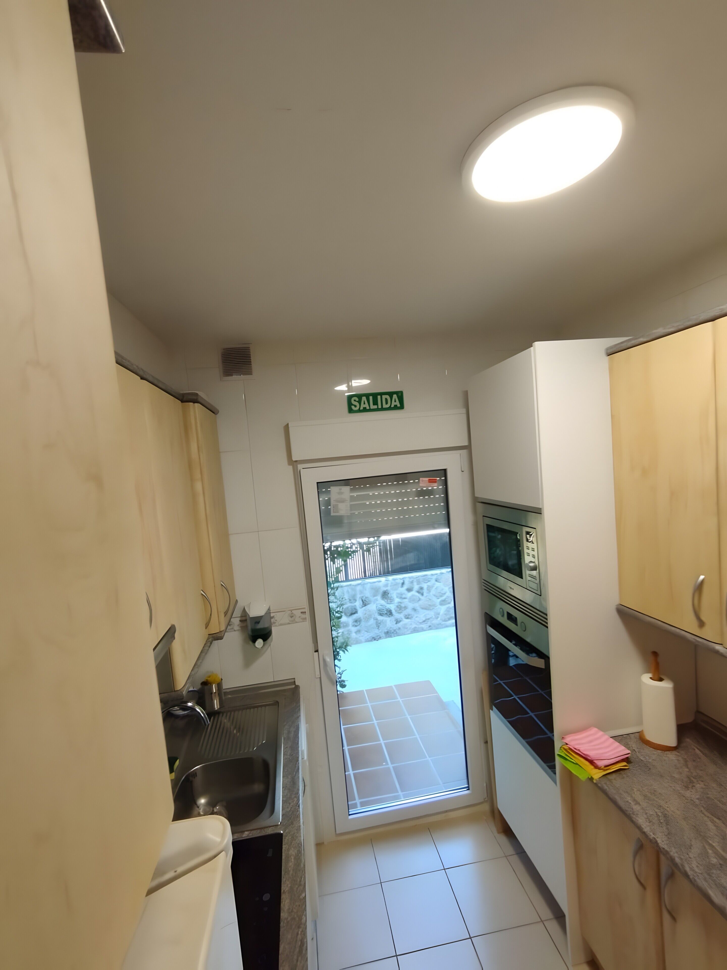 A narrow kitchen with a sink, cabinets, a microwave, and a sign indicating an exit.