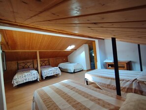 Una habitació amb tres llits, bigues de fusta al sostre i teulada inclinada.