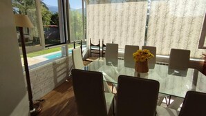 Comedor con una mesa de vidrio, sillas, un florero con flores y vista a una piscina.