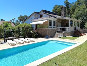 Piscina amb gandules, edifici de pedra amb un balcó i cel blau clar.