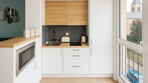 A modern kitchen with white cabinetry, a black and white backsplash, and a view of a church through a large window. - Charmant T2 lumineux près de Montmartre (Paris)