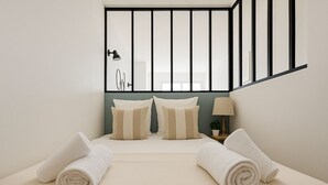 A hotel room with a bed, two pillows, a nightstand with a lamp, and a view of a staircase. - Charmant T2 lumineux près de Montmartre (Paris)