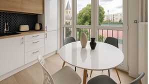 A modern kitchen with white cabinets, a wooden countertop, and a large window offering a view of a building and trees. - Charmant T2 lumineux près de Montmartre (Paris)